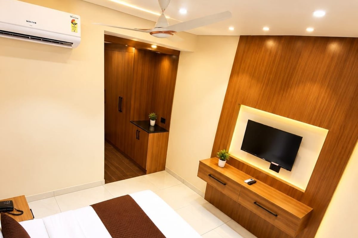 Moderni hotellihuone, jossa on suuri sänky, televisio, kattotuuletin ja puinen vaatekaappi.