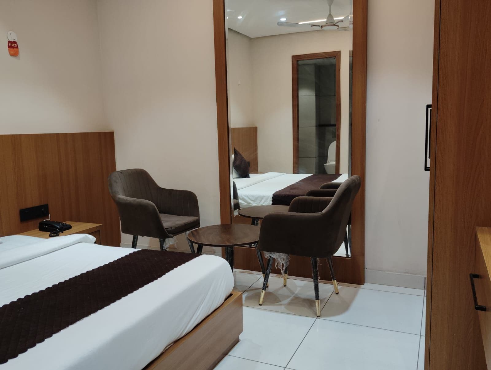 A hotel room with a bed, two armchairs, a small table, and a mirror reflecting a bathroom.