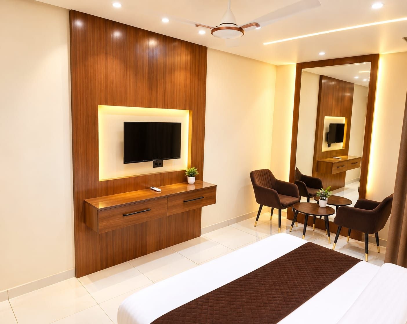 Habitación de hotel con cama, televisor montado en un panel de madera, escritorio con silla, mesita con planta y espejo.