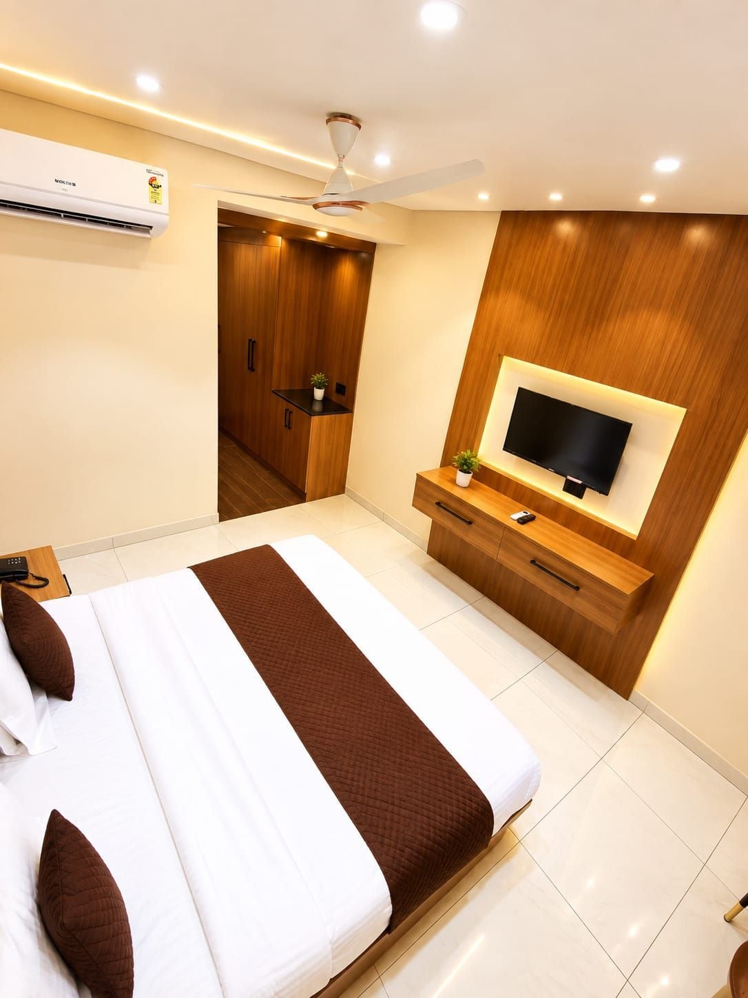 Habitación de hotel moderna con una cama grande, televisor, ventilador de techo y armario de madera.