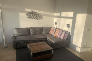 A modern living room with a sectional sofa, a wooden coffee table, and a wall-mounted light fixture. - Sunset 72 - House Berlin (Großenbrode)