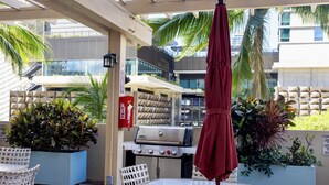 En udendørs terrasse med bord, stole, grill og potteplanter.