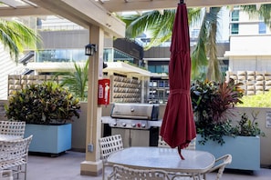 An outdoor patio with a table and chairs, a grill, and potted plants. - Luxury Waikiki 1BR: Ocean View & Free Parking (Honolulu)