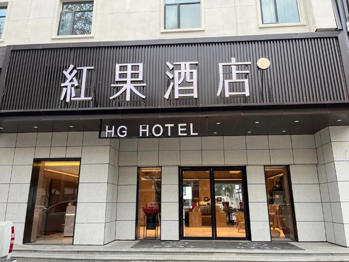 Een hotelentree met een bord waarop 'HG Hotel' staat en een groot bord erboven met de tekst 'Red Apple Hotel'.