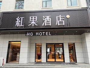 Entrada de un hotel con un letrero que dice 'HG Hotel' y un cartel grande encima que indica 'Red Apple Hotel'.