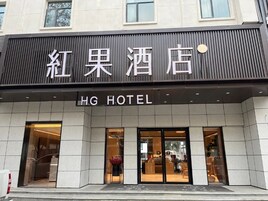 Entrada de un hotel con un letrero que dice 'HG Hotel' y un cartel grande encima que indica 'Red Apple Hotel'.
