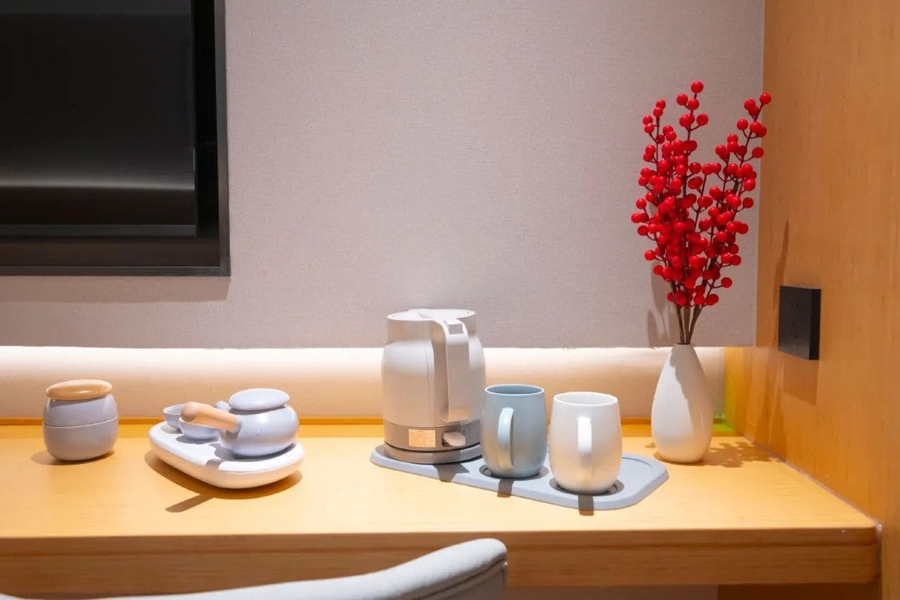 A neatly arranged breakfast area with a coffee maker, cups, and a vase with red berries.