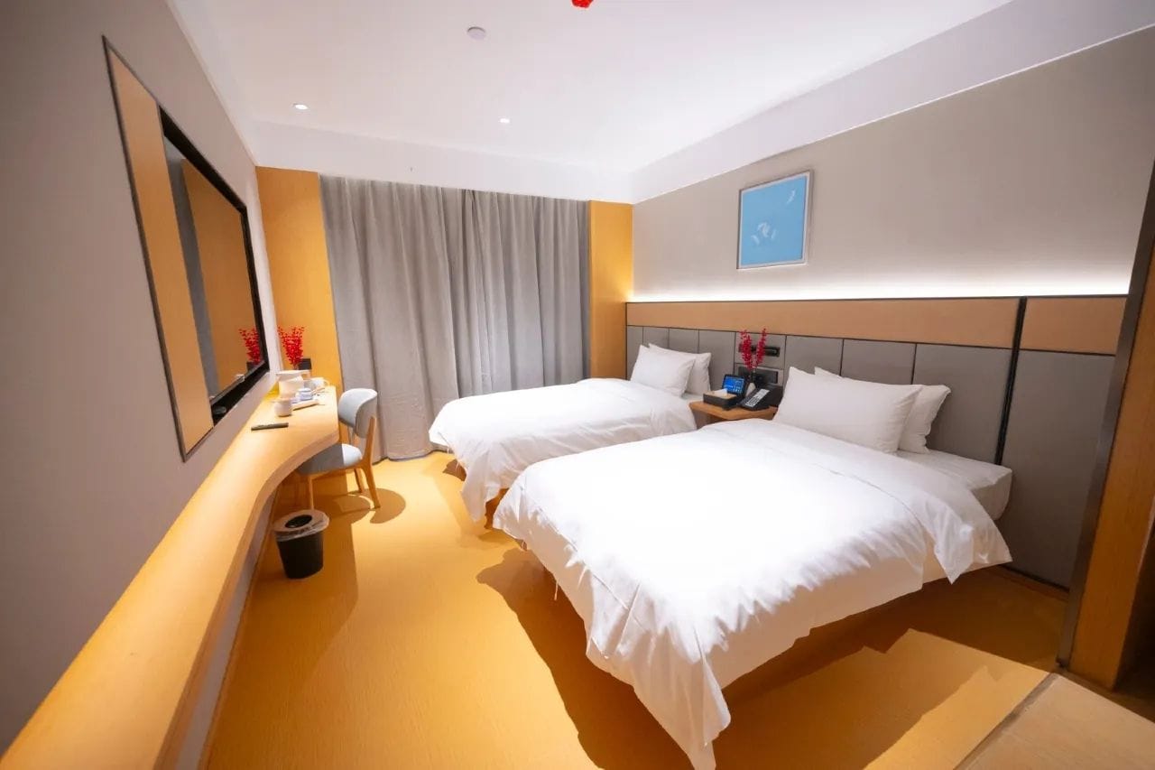 A hotel room with two beds, a desk, a chair, a bedside table, and a large mirror.