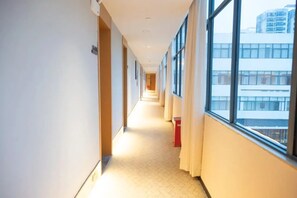 Pasillo de hotel con suelo de baldosas, ventanas grandes y un cubo de basura rojo.