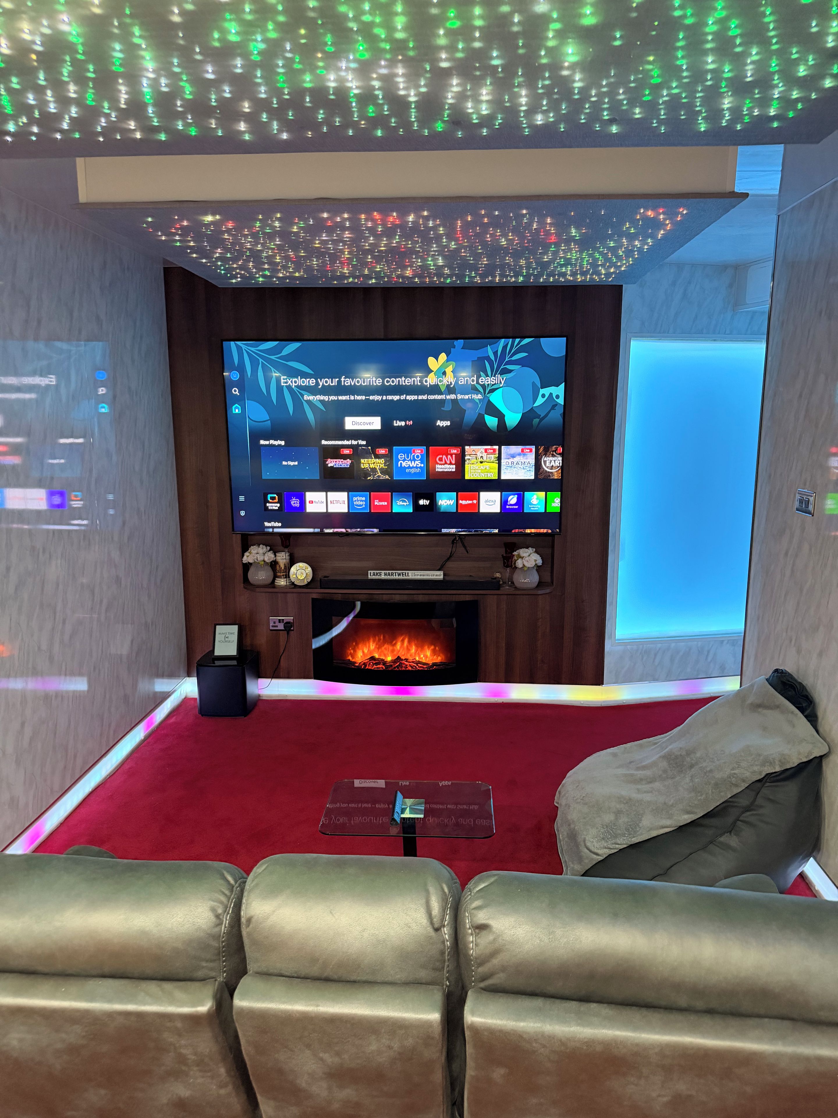 Un salon moderne avec un téléviseur à écran plat, une cheminée, des canapés en cuir et une moquette rouge.