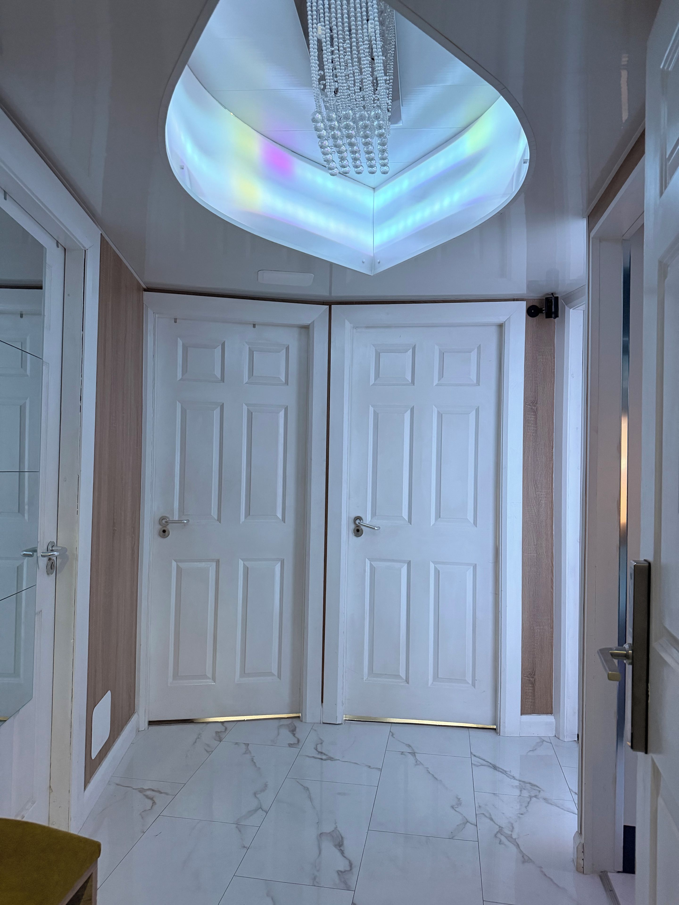 Una habitación con dos puertas blancas, piso de mármol y una lámpara en el techo.