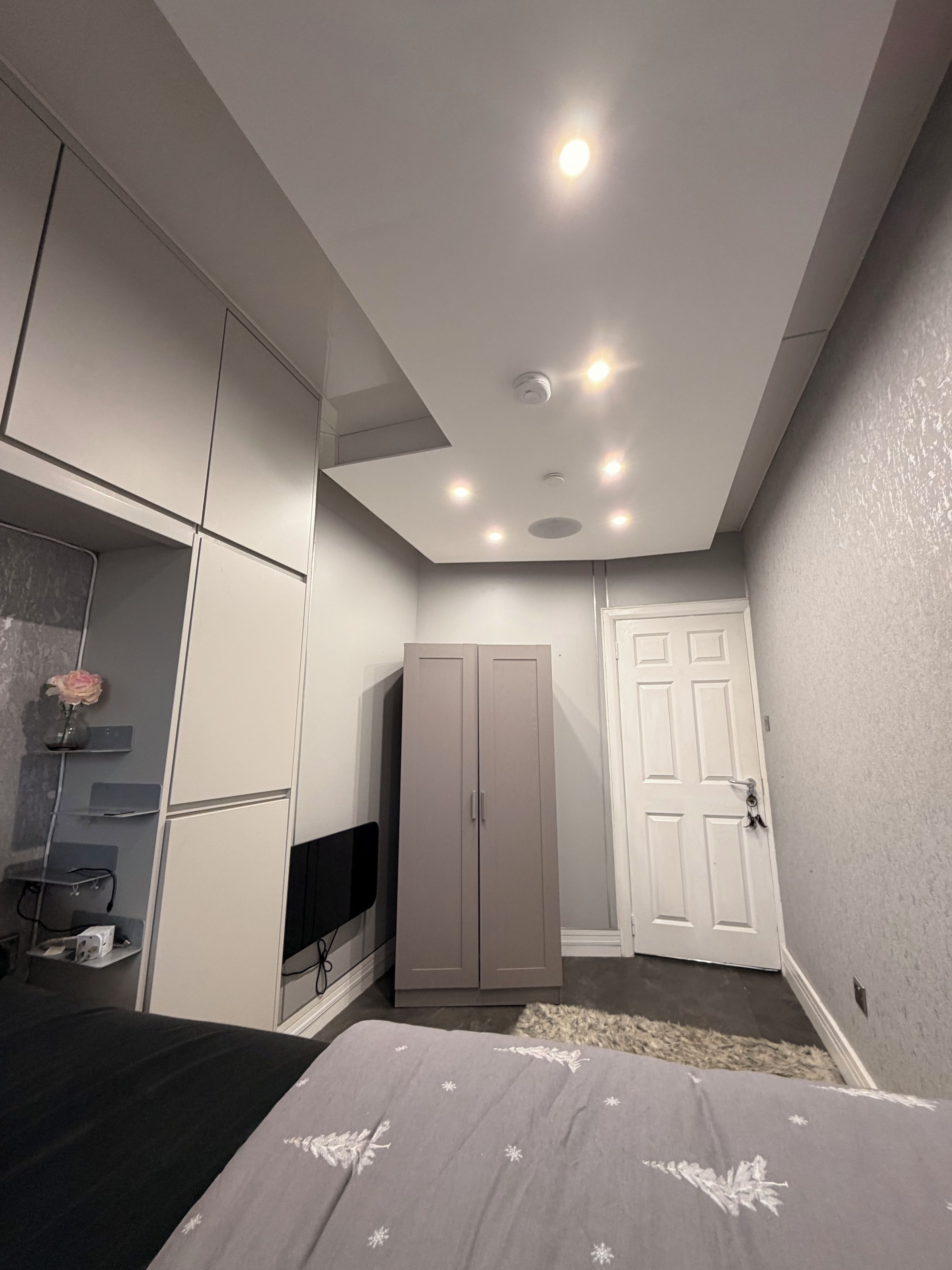 A bedroom with a bed, wardrobe, TV, and a door.