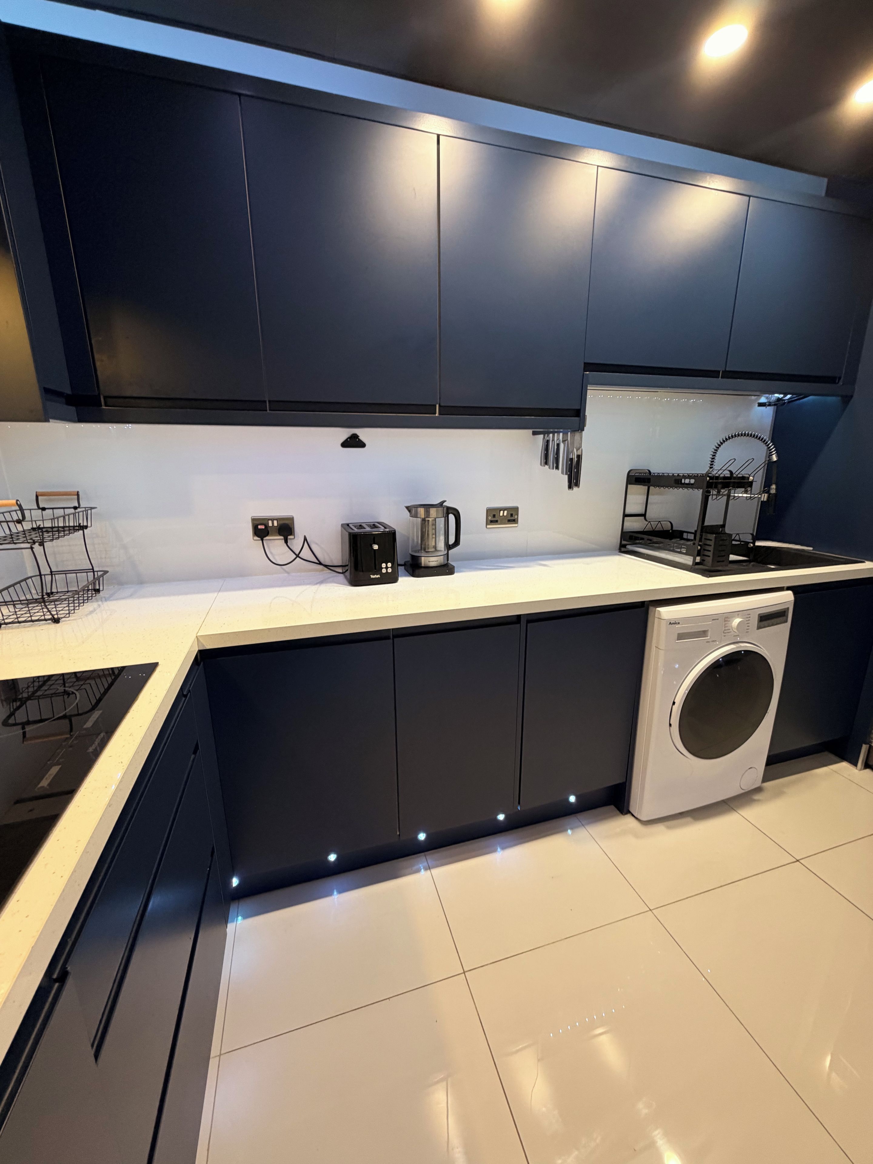 Een moderne keuken met donkere kastjes, een ingebouwde wasmachine en een aanrecht met koffiezetapparaat en broodrooster.