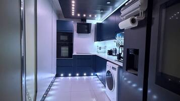 A modern kitchen with a built-in washer and dryer, recessed lighting, and a flat-screen TV mounted on the wall.