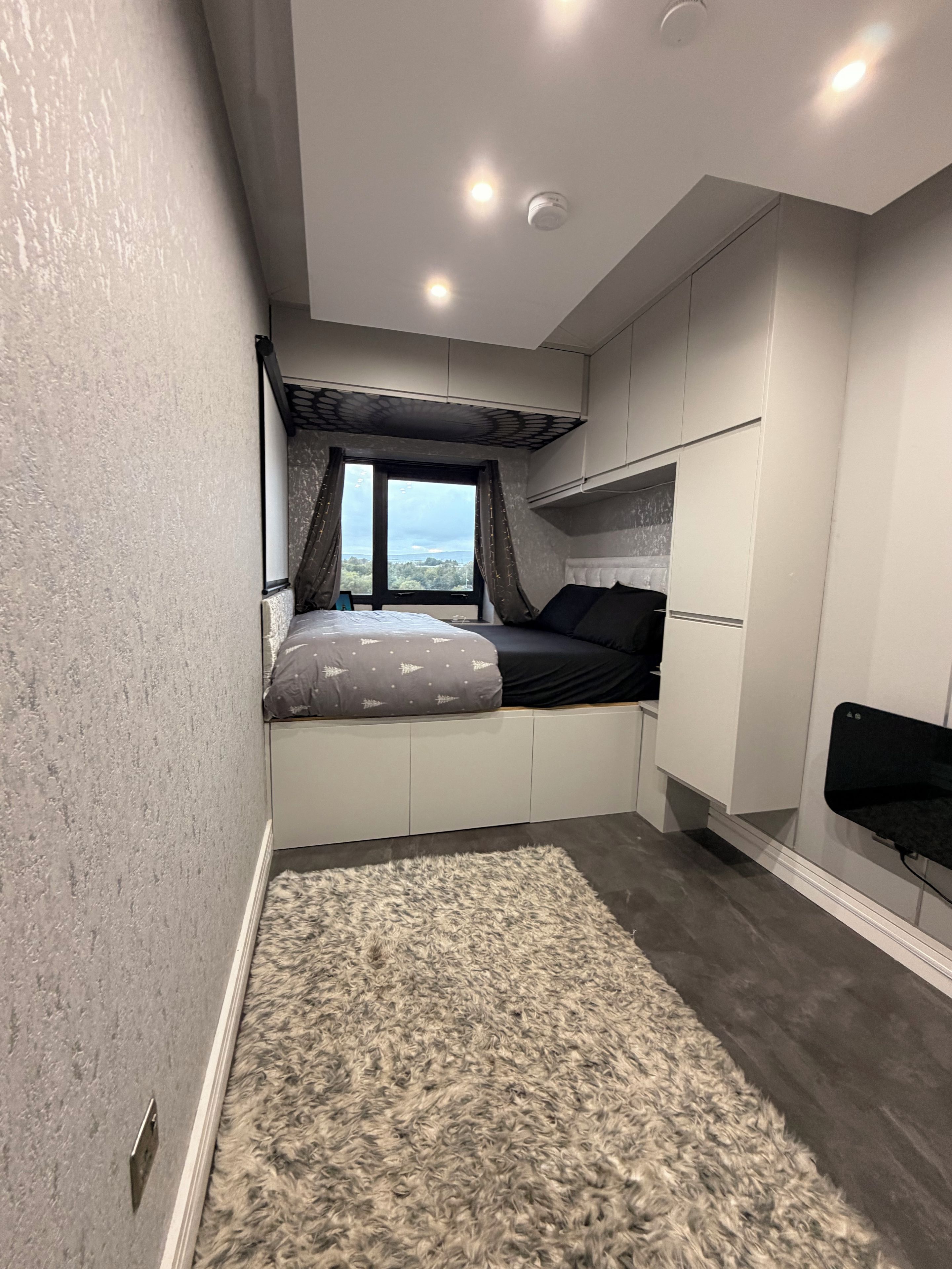 A bedroom with a bed, a window, built-in storage, and a small seating area.