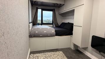 A bedroom with a bed, a window, built-in storage, and a small seating area.