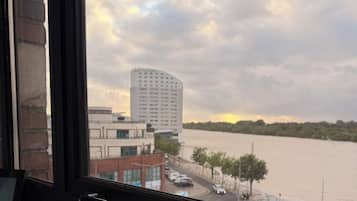 Uitzicht door een raam op een gebouw, met een rivier en een hoog gebouw op de achtergrond.