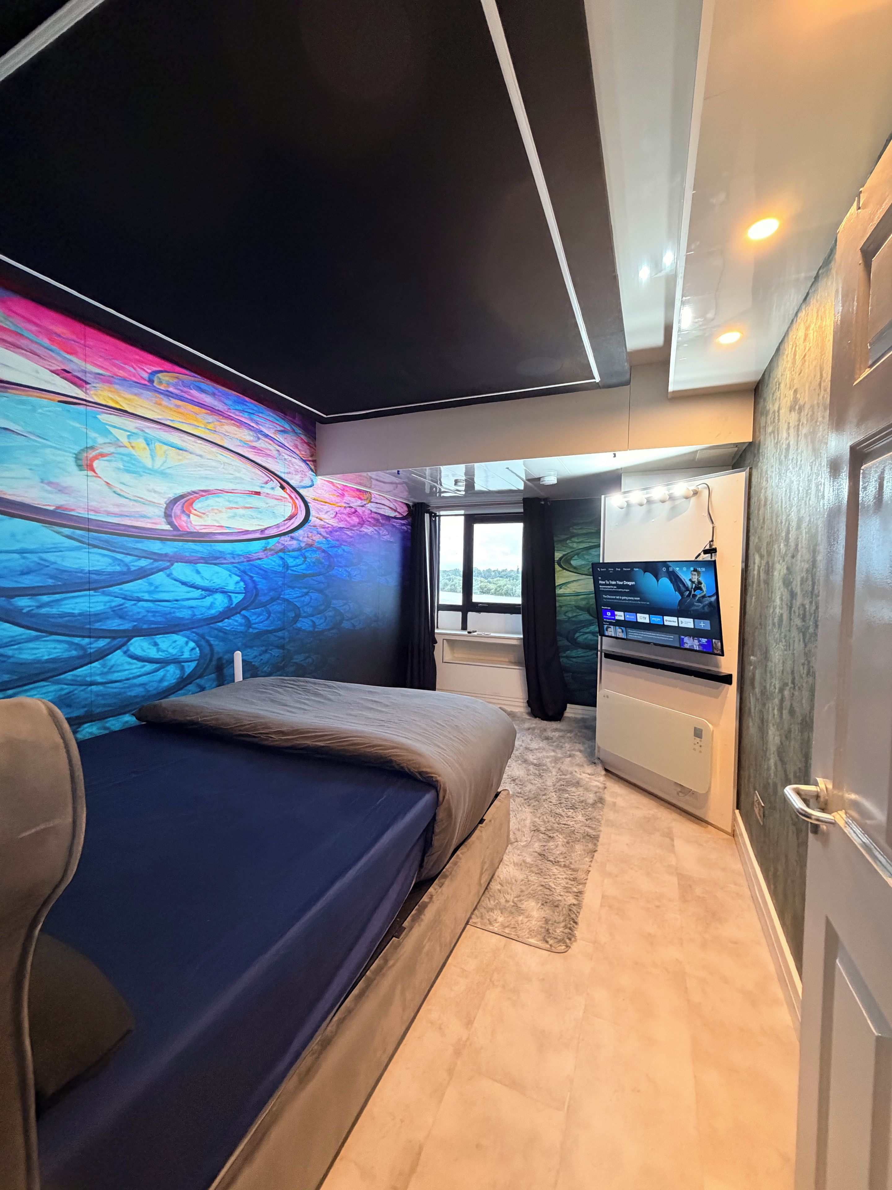 A modern bedroom with a large bed, a television, and a colorful mural on the wall.
