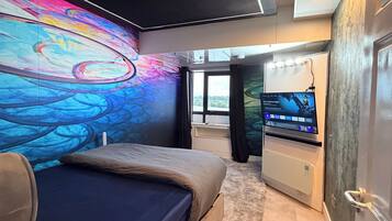 A modern bedroom with a large bed, a television, and a colorful mural on the wall.