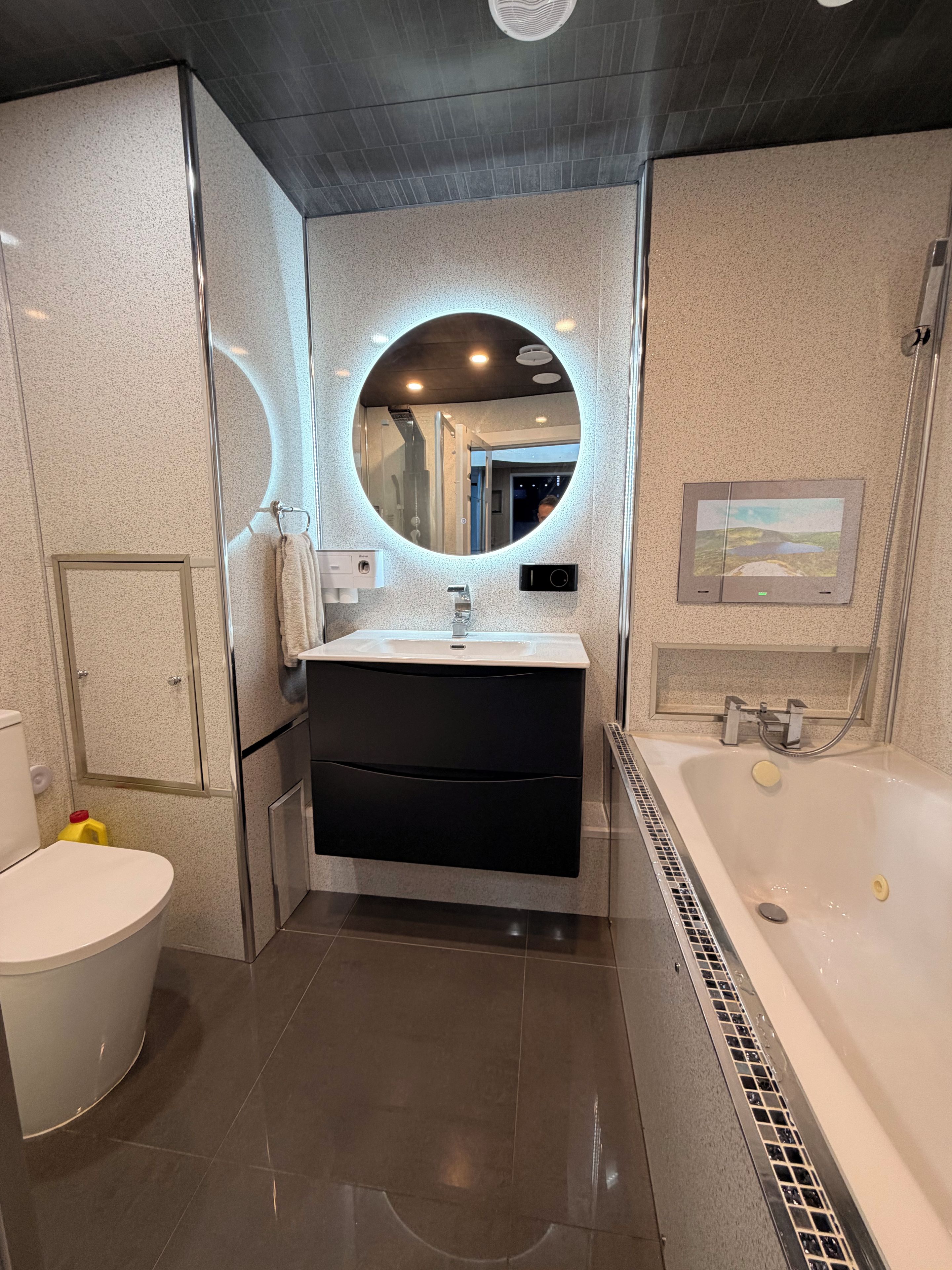 A modern bathroom with a round mirror, a bathtub, and a toilet.
