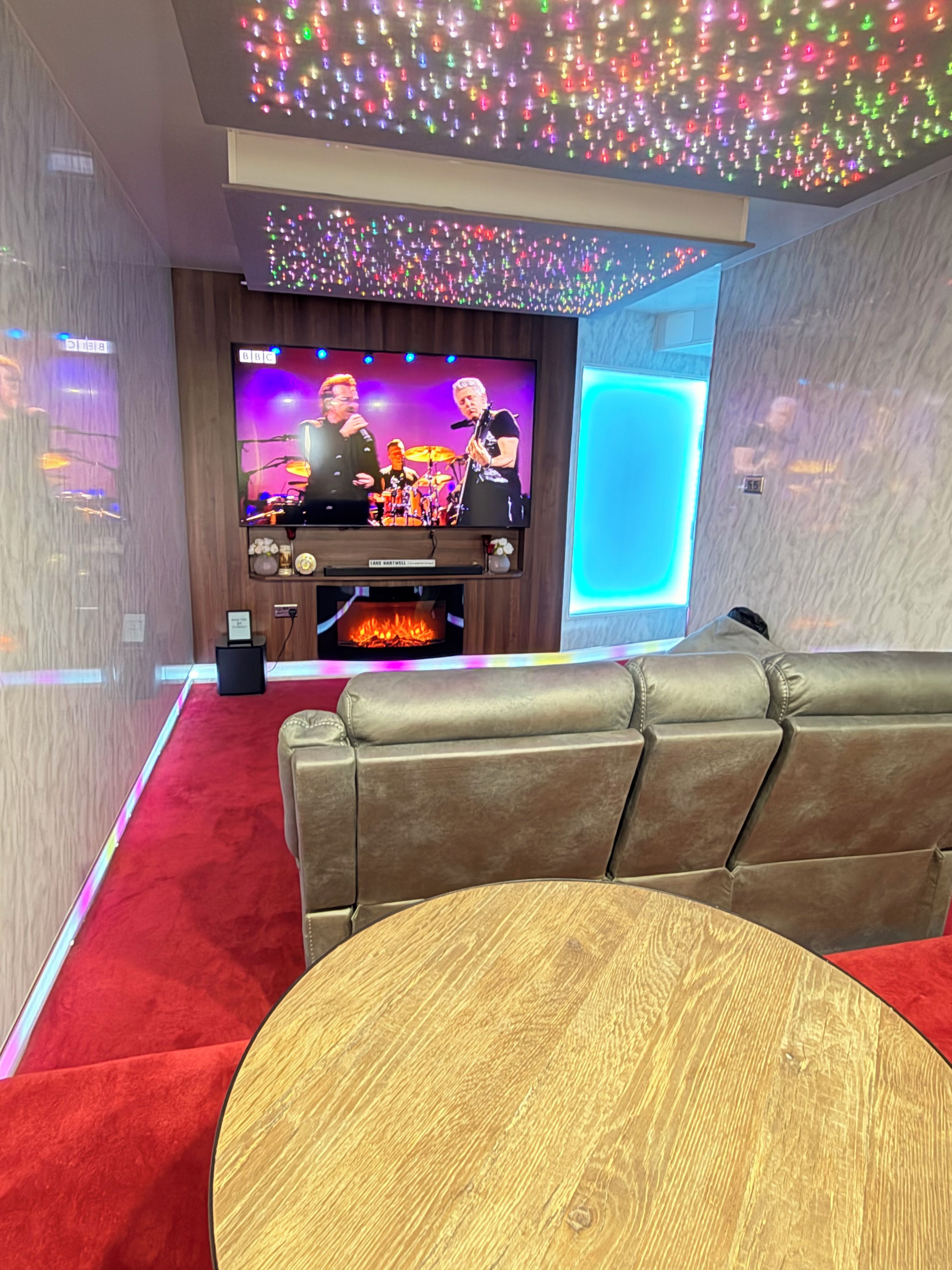 A modern living room with a flat-screen TV, leather sofa, and a round wooden table.