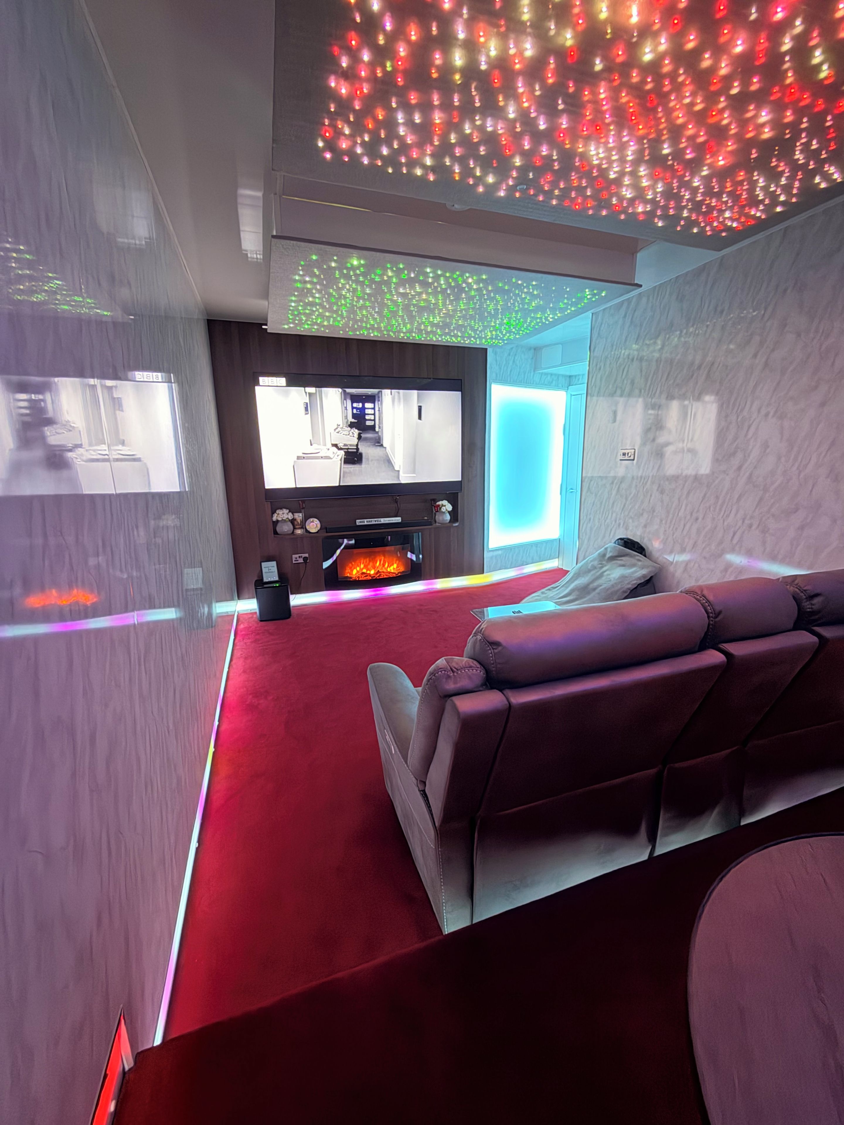 Een moderne woonkamer met een rood tapijt, leren bank, flatscreen televisie, open haard en sfeerverlichting.