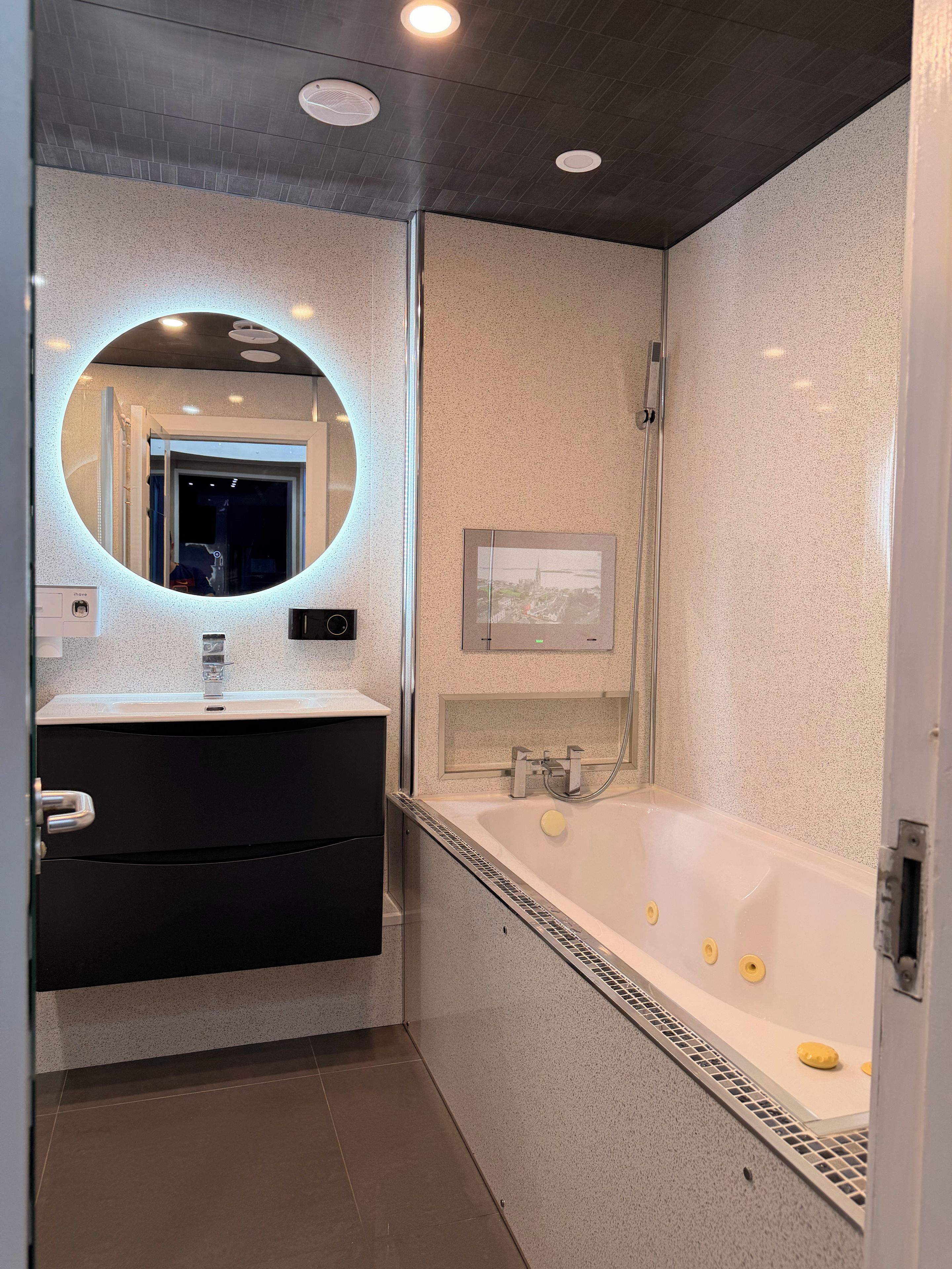 Un baño moderno con un espejo redondo, una bañera y una ducha.