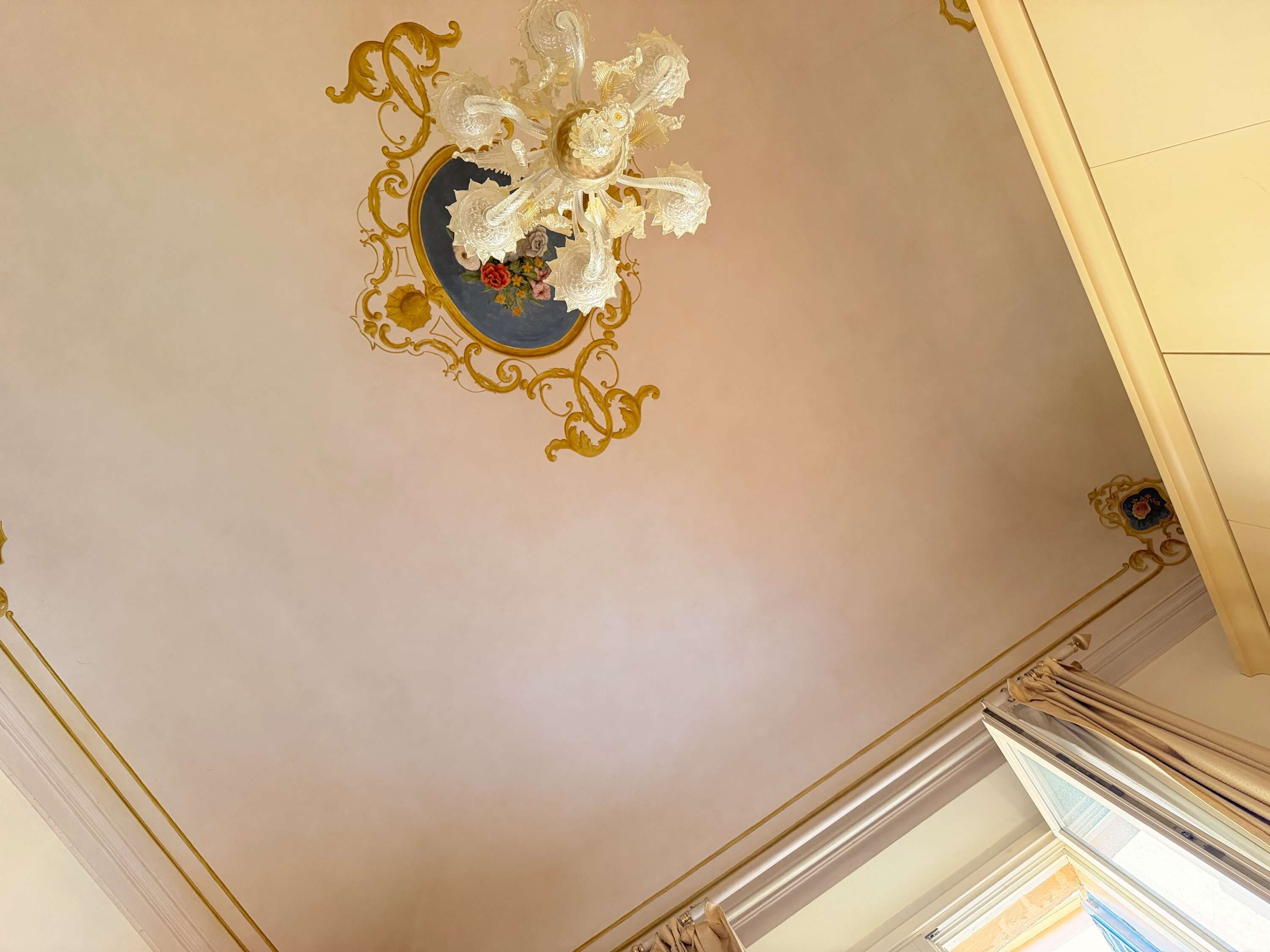 Eine Decke mit einem dekorativen Chandelier und aufwendigen Goldverzierungen.