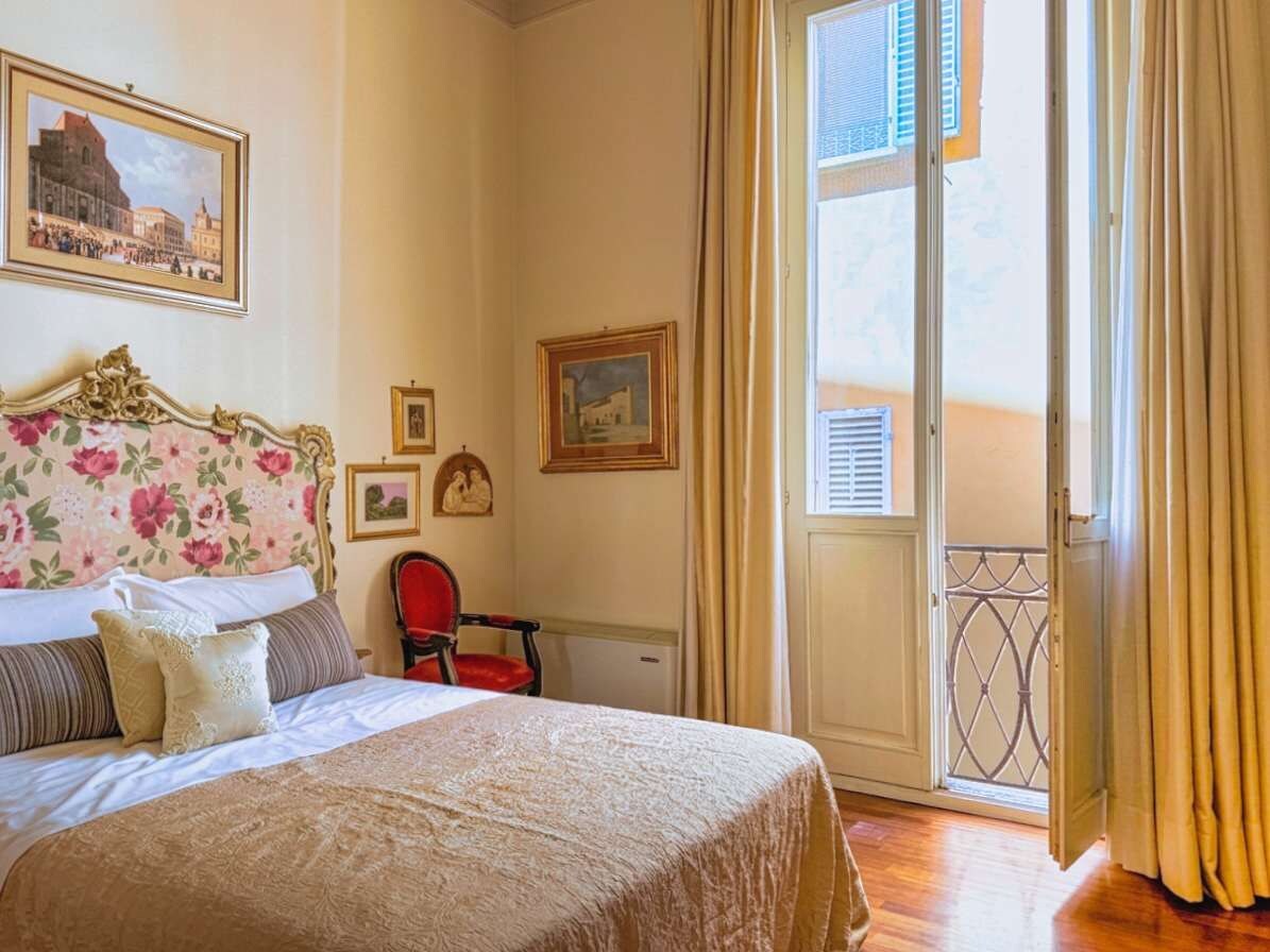 A hotel room with a bed, a chair, a balcony, and a door.