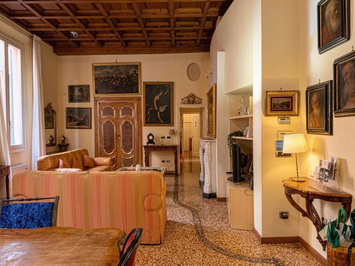 A hotel room with a sofa, a wooden ceiling, framed artwork on the walls, and a lamp on a side table.