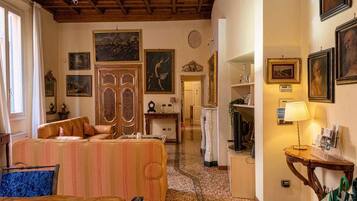 A hotel room with a sofa, a wooden ceiling, framed artwork on the walls, and a lamp on a side table.