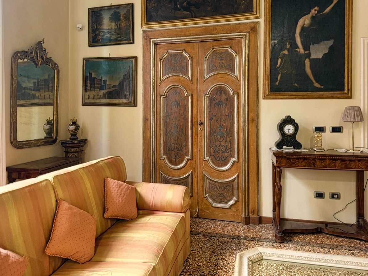 A room with a sofa, a wooden door with decorative panels, a clock, and framed artwork on the walls.