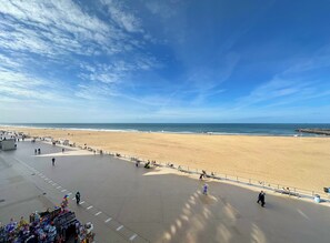 Ein Strand mit gepflastertem Weg, einer Umzäunung und blauem Himmel.