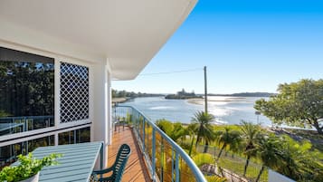 A balcony with a view of a river and a bridge, a table with a plant, and a chair.