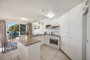 A modern kitchen with white cabinets, a central island, and a dining area with a view to the outside. - Charming 2-bed Coastal Haven Near Esplanade (Sunshine Coast)