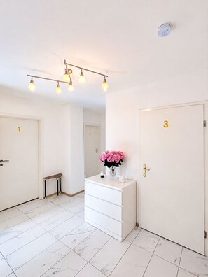 A hotel room with a marble-tiled floor, a white dresser with a vase of flowers, and three doors numbered 1, 2, and 3.