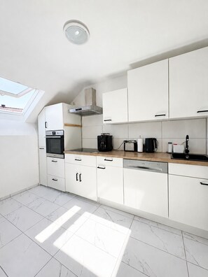 A modern kitchen with white cabinets, a built-in oven, a coffee maker, and a skylight.