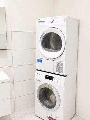 A stacked washer and dryer unit in a bathroom with white tiles.