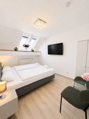 A modern bedroom with a bed, bedside table, lamp, TV, and a desk with a chair.