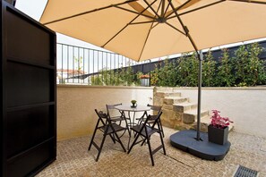 An outdoor patio with a table and chairs under a large umbrella, surrounded by stone steps and potted plants. - URBAN CABIN (Vila Nova de Gaia)