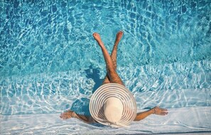 Uma pessoa deitada à beira da piscina com os pés na água, usando um chapéu.