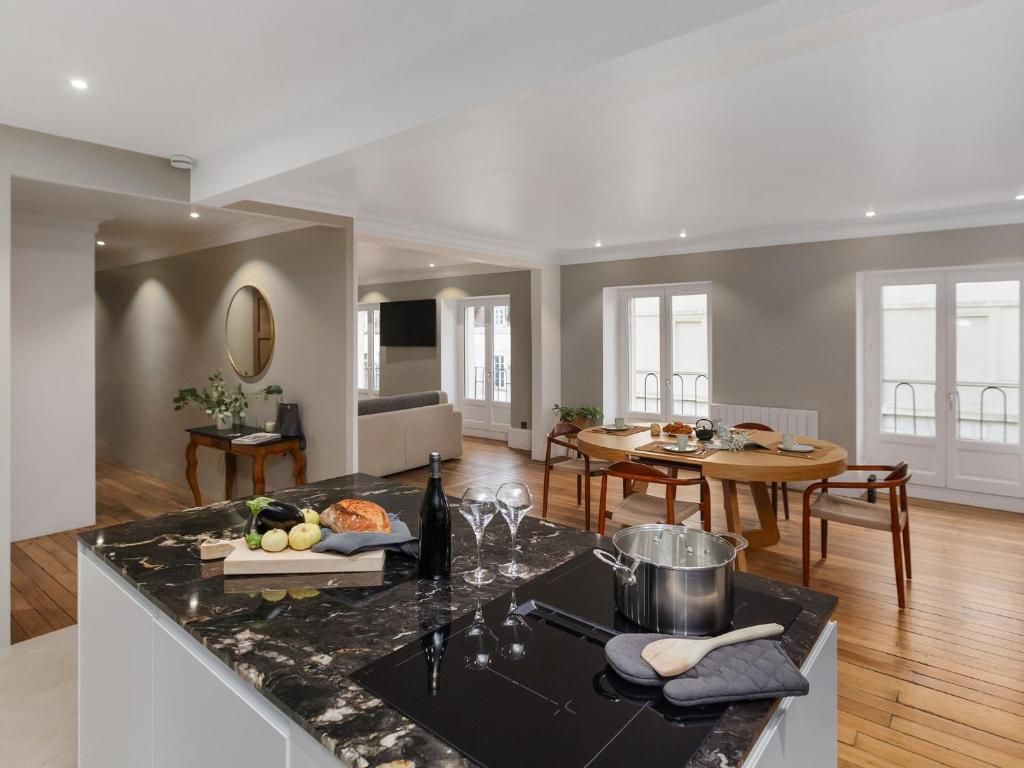 Una cocina moderna con encimera de mármol, comedor con mesa redonda y vistas al exterior a través de amplias ventanas.