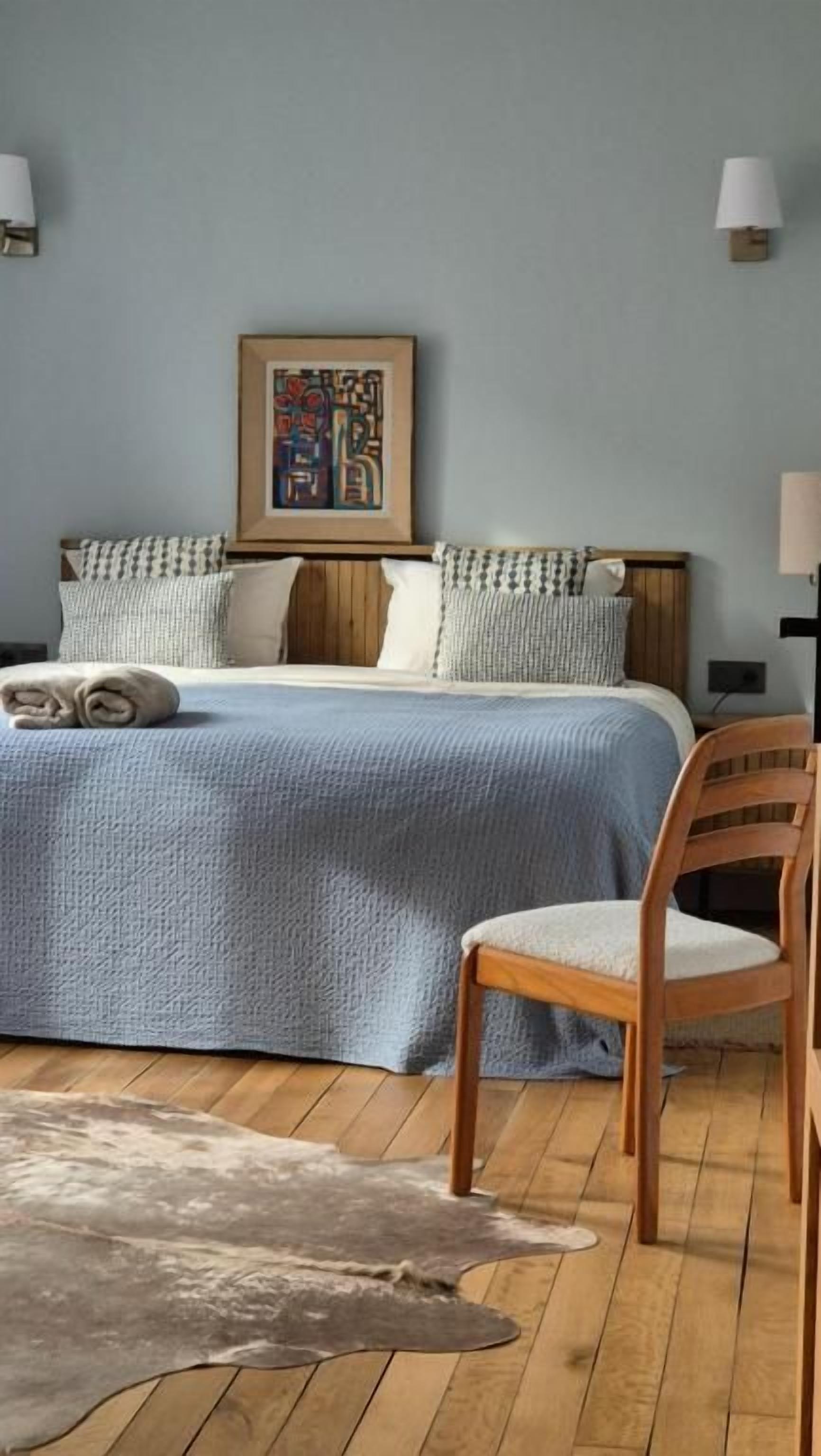Ein Schlafzimmer mit einem Bett, Kissen, einem Sessel, einem Teppich und einem Wandbild.