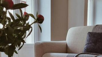 A room with a sofa, a table with a book and two mugs, and a window with a plant.