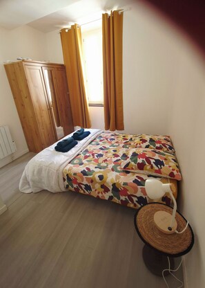 Un dormitorio con cama, armario, ventana con cortinas y una lámpara de noche.