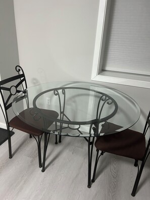 A round glass table with metal legs and two chairs, positioned near a window with blinds. - Charming & Peaceful Home Away From Home (Calgary)