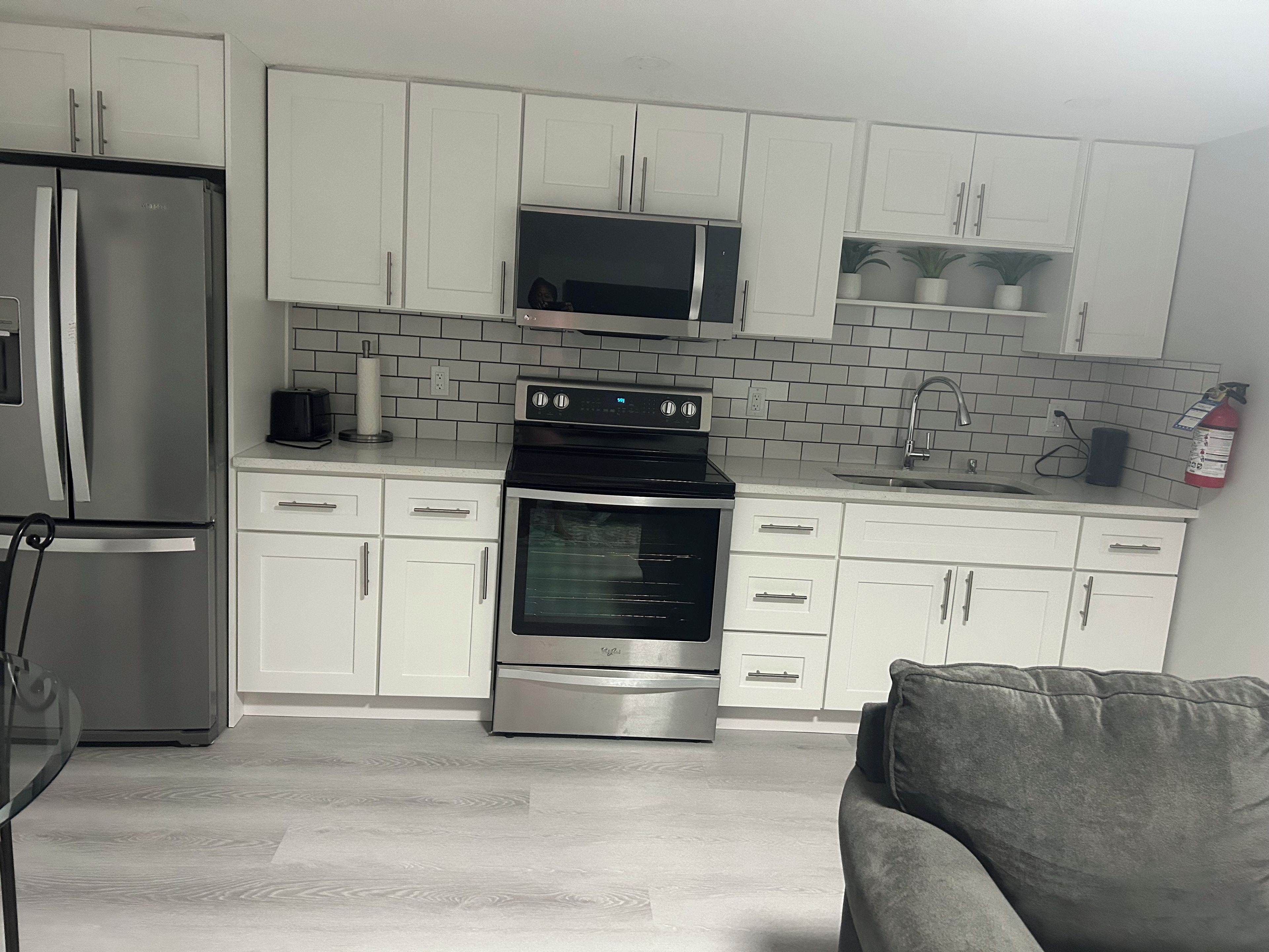 A modern kitchen with white cabinets, a stainless steel refrigerator, a microwave, an oven, and a sink.