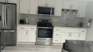 A modern kitchen with white cabinets, a stainless steel refrigerator, a microwave, an oven, and a sink.