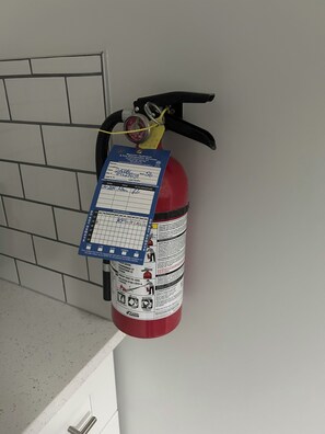 A fire extinguisher mounted on a wall with a label and a pressure gauge. - Charming & Peaceful Home Away From Home (Calgary)