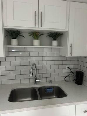 A kitchen with a double sink, white cabinets, and potted plants on a shelf. - Charming & Peaceful Home Away From Home (Calgary)